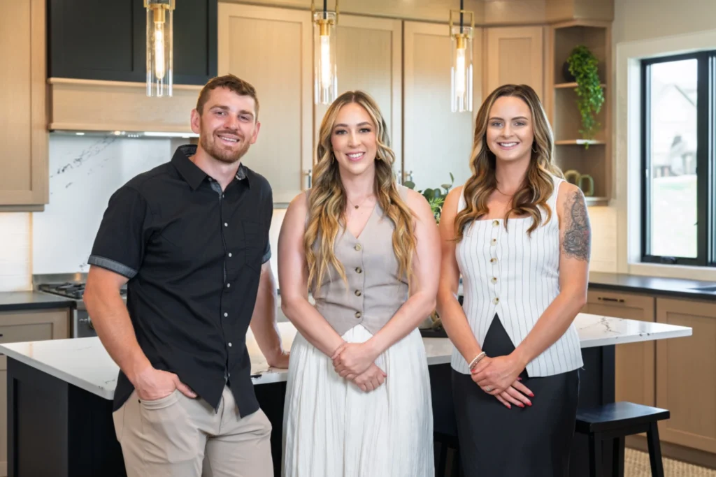 The Premier Team at D.Y.C. Realtors in Great Falls, Montana — Paul Brannan, Ambyr Rain Showers, and Audrey Lazzarini standing together in a modern kitchen